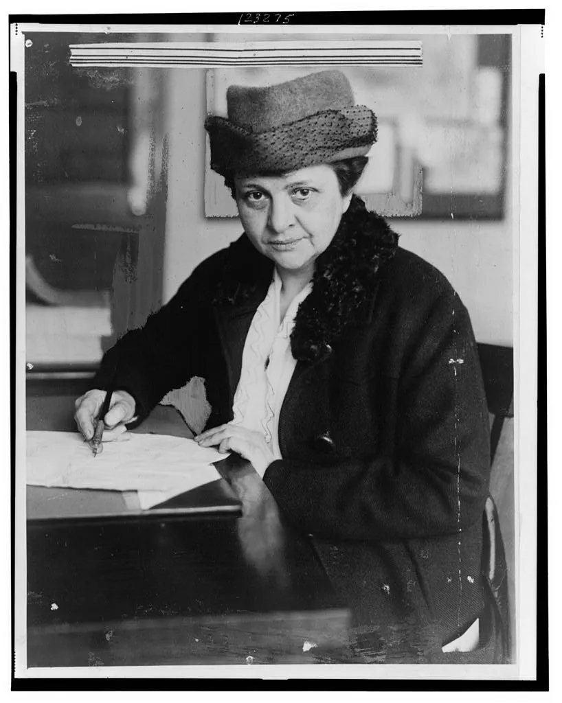 Woman with a hat on looking into the camera and holding a pen