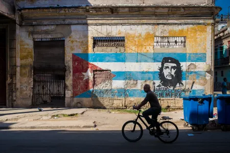 A cyclist rides past a colorful mural, featuring the Cuban flag and an image of Guevara.
&nbsp;