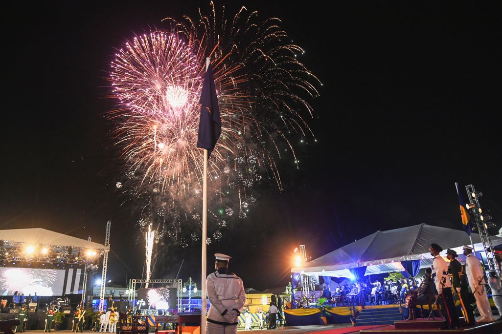 Fireworks illuminate the night sky behind a Barbadian national flag