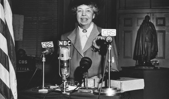 Eleanor Roosevelt standing in front of four microphones labeled as CBS and NBC