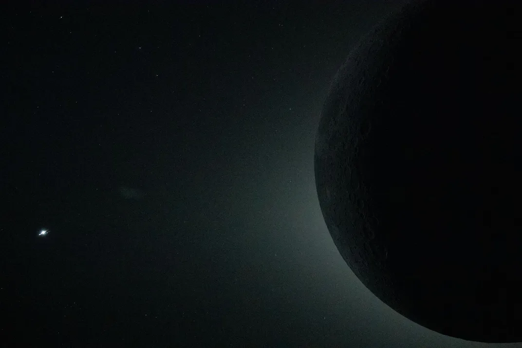 a dark orb of the moon is at the right, with a light haze around it. a bright spot at the left is Venus