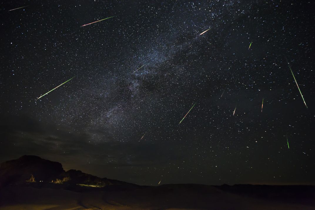 Green, red and multicolored shooting stars appear to radiate from the same spot in a very dark night sky