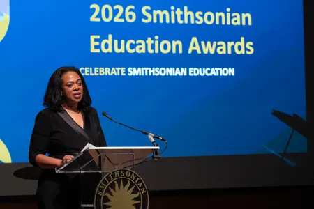 A women stands at a podium in front of a bright blue background