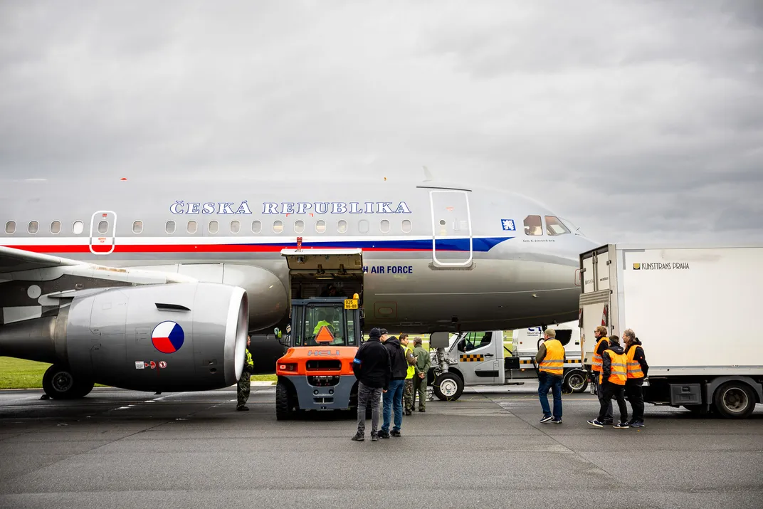 a Czech airplane on the runway, with people in orange vests standing around it