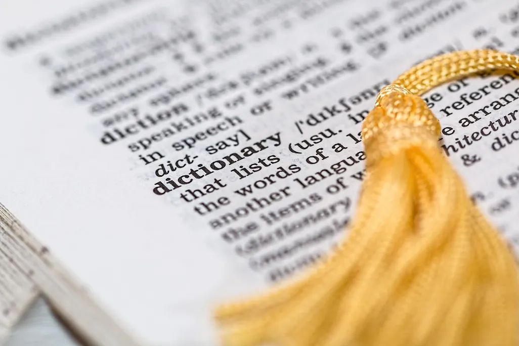 The page of a dictionary open to the word "dictionary" with a yellow tassel on top of the page