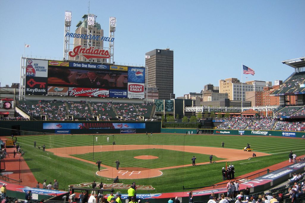 A view of a baseball field, with Indians written in red lettering above the scoreboard and crowds filling the stands