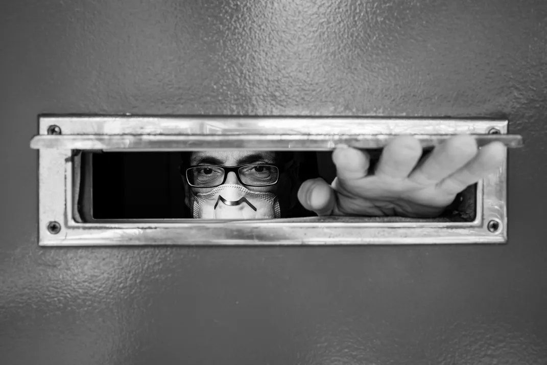 A man with a face mask looks through his mail slot