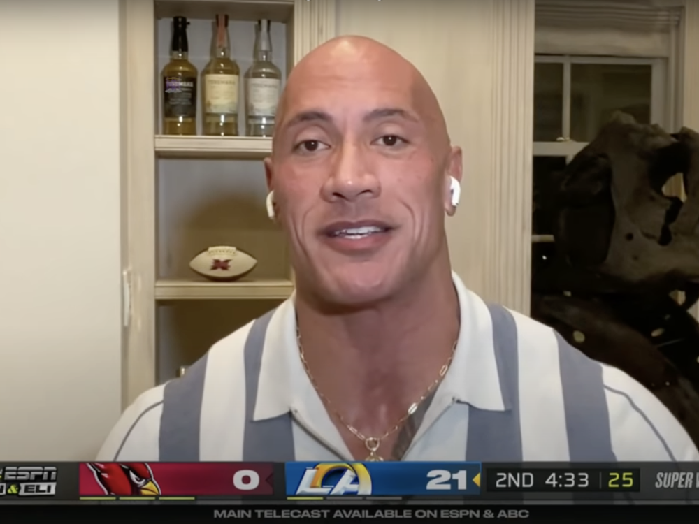 An image of Dwayne "The Rock" Johnson in a virtual call for ESPN's "ManningCast" show. Behind the actor is a T.rex skull.
