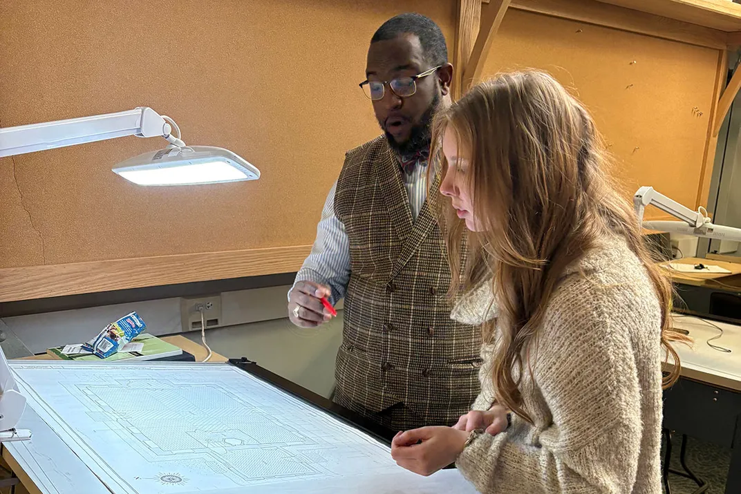 Two people inspect something out of frame. One holds a pen and looks surprised.