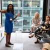 Summer Hamilton stands at a podium in front of a room full of people. She is slightly turned and pointing towards something on the wall behind her.