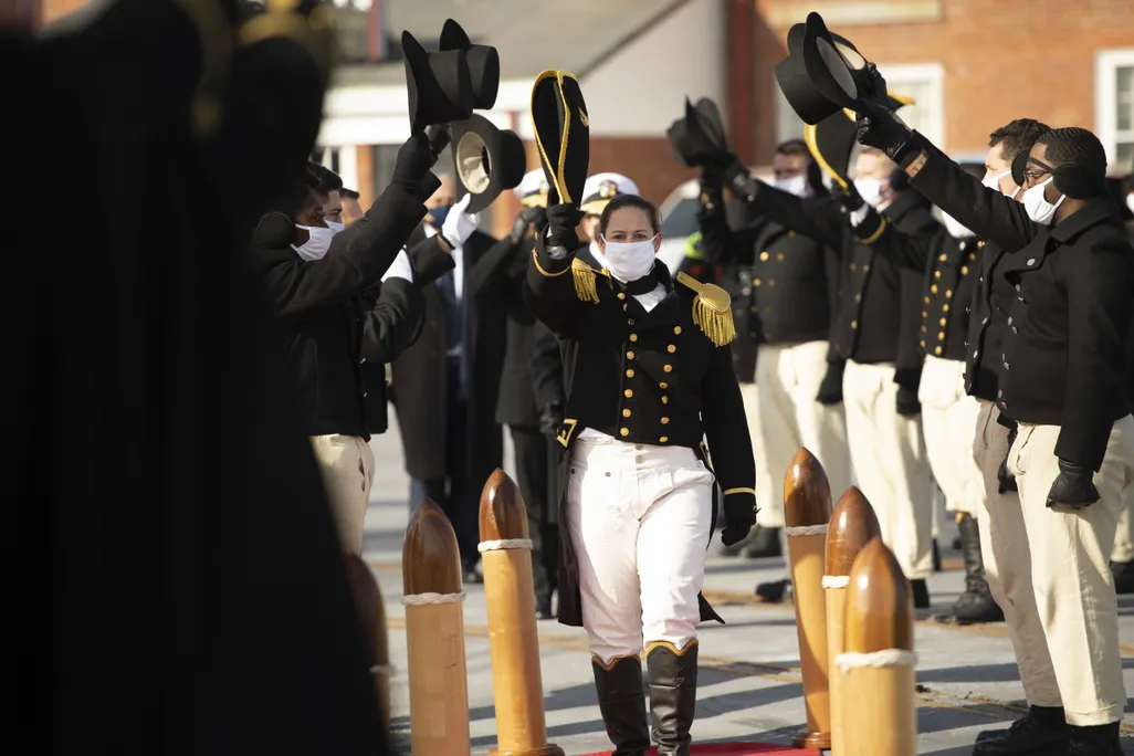 woman in black navy dress uniform being saluted by two rows of fellow sailors