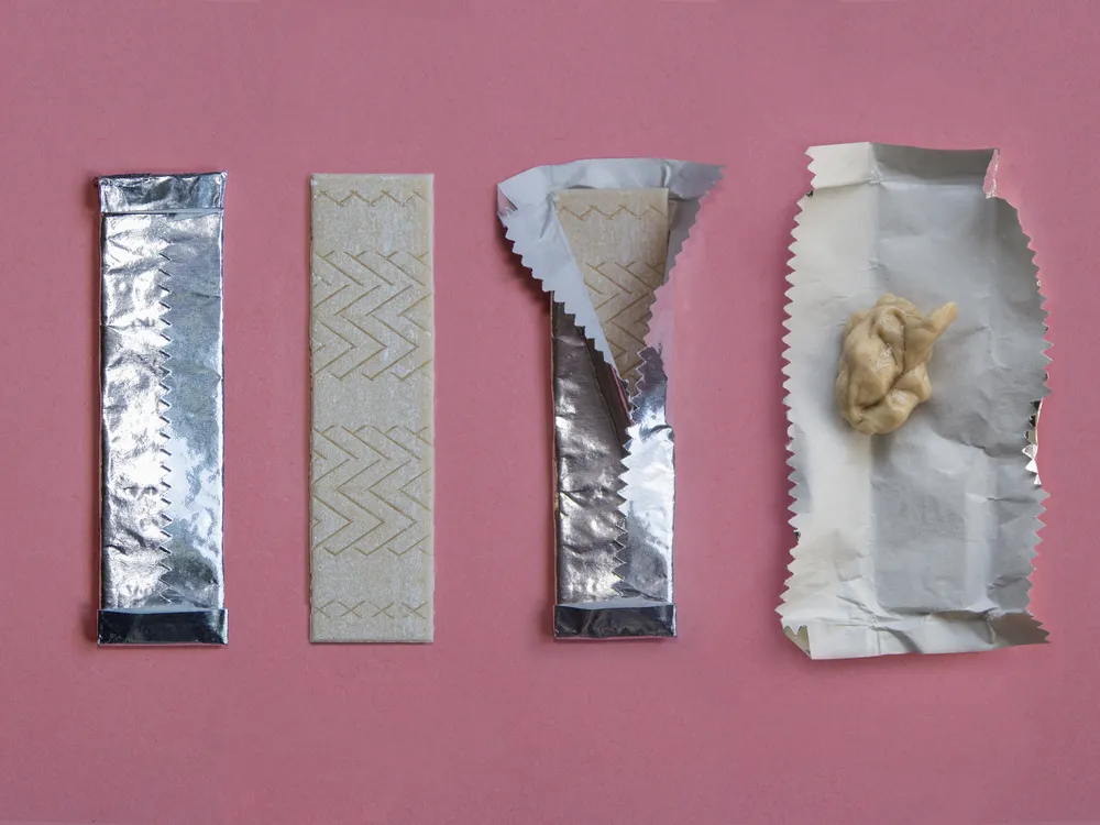 An image of a stick of gum shown in the stages of being used. Starting with unwrapping the stick of gum to ending with sticking the used piece in its foil wrapper. The sequence is shown against a pink background.