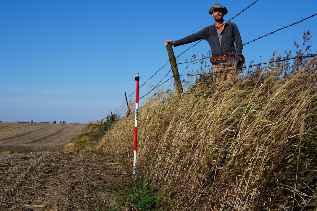 An image of a reseacher standing on native prairie a few feet above degraded farmed land.