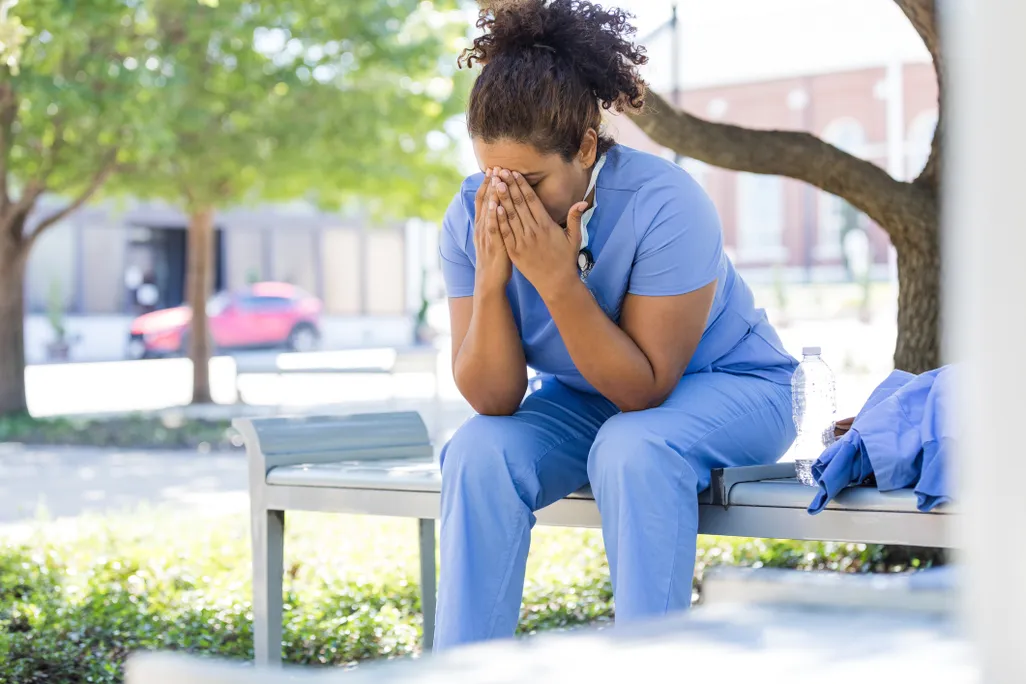 A healthcare worker sits outside with her head in her hands