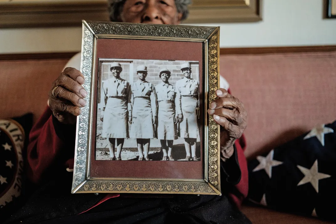 A Black woman holds up a group photo of herself and friends in uniform during world war two