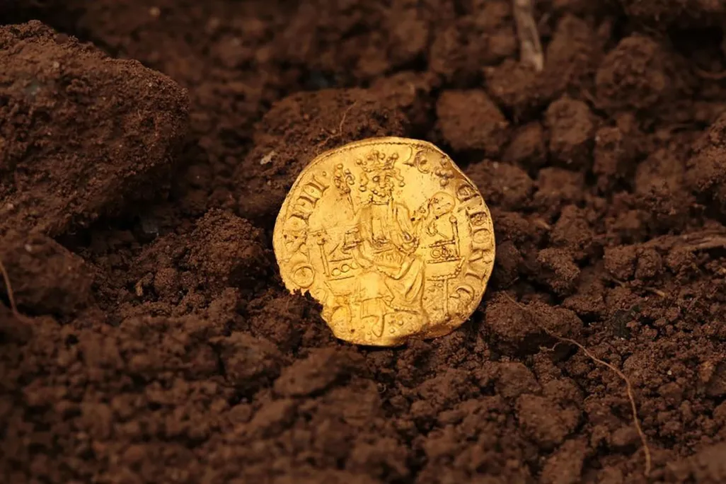 bright gold coin in dirt depicting crowned and bearded man