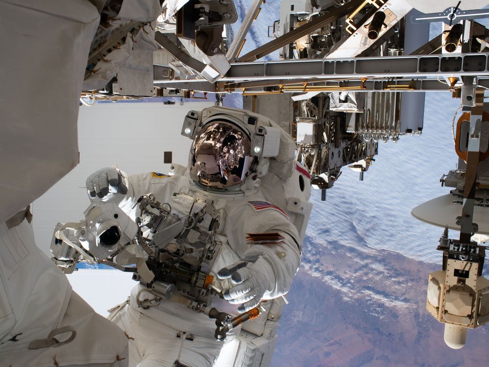 An astronaut tethered to the outside of the International Space Station, with a view of Earth behind.