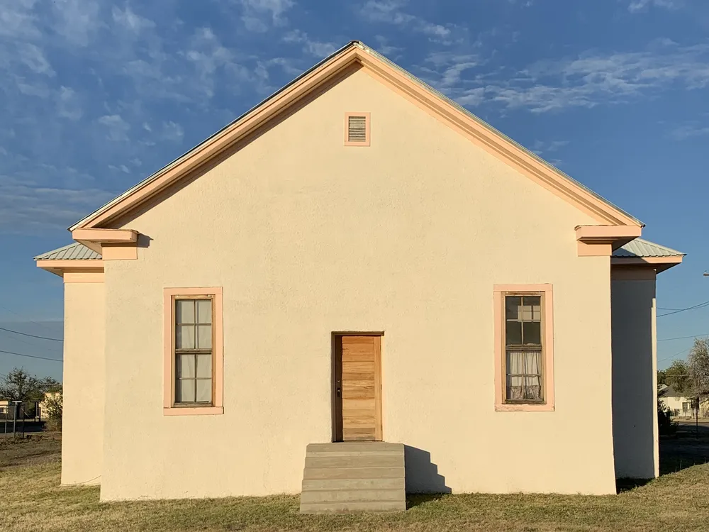 A front-on view of a simple white building with two windows on either side of a small door