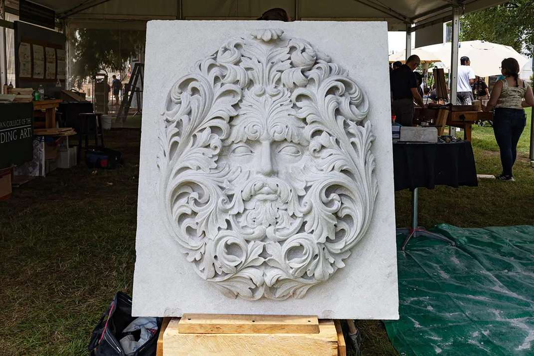 A four- or five-foot tall slab of white stone with the face of a man in swirling foliage chiseled into the surface.