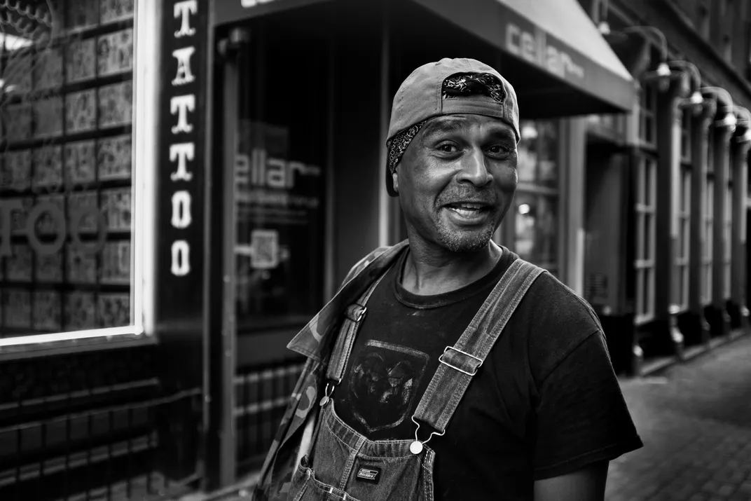 A black and white photo of an older Black man outside a tattoo shop