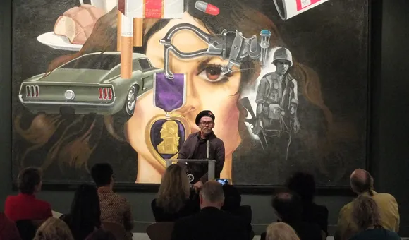 Jesse Treviño speaking in front of guests. His artwork "Mi Vida" is projected behind him.