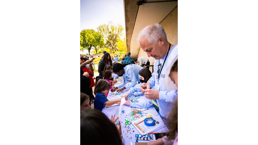 Photo of a table surrounded by a crowd. The table is filled with colorful LED lights, batteries, tape, and scissors.