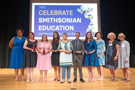 A group of people posing for a photo on a stage.  Dr. Monique M. Chism with Awardees and Smithsonian Women’s Committee supporters at the 2022 Smithsonian Education Awards Ceremony, July 28, 2022.