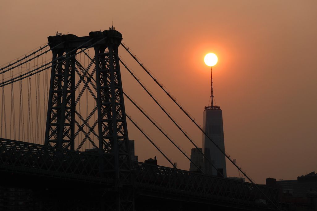 The sun sets behind the Manhattan Bridge and One World Trade Center in a haze created by smoke