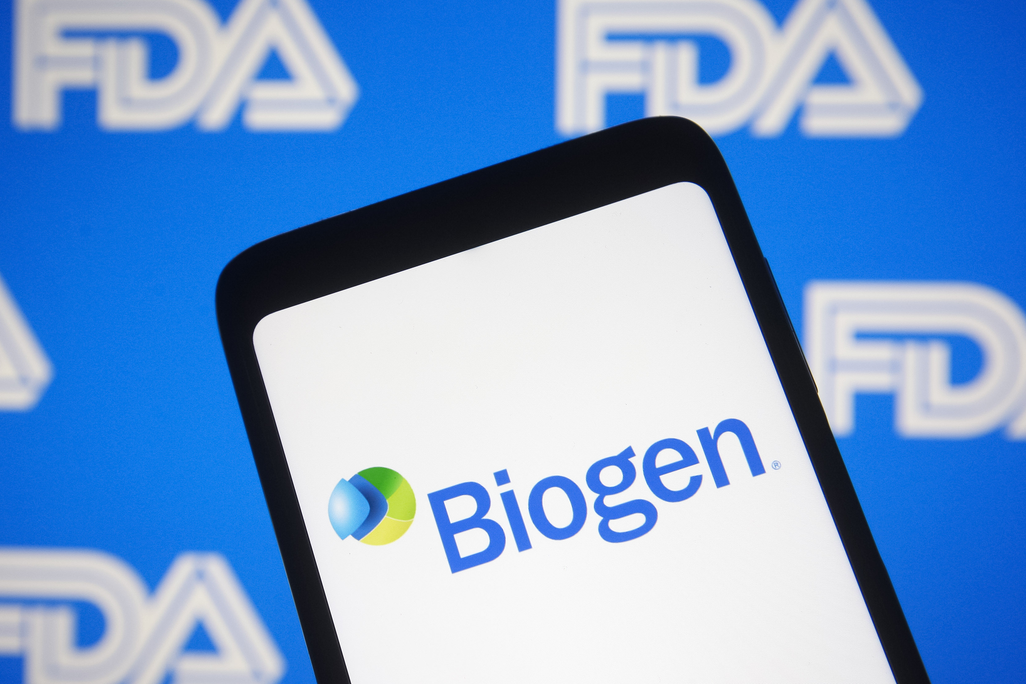 A phone screen shows the Biogen logo in front of a background with the FDA logo 