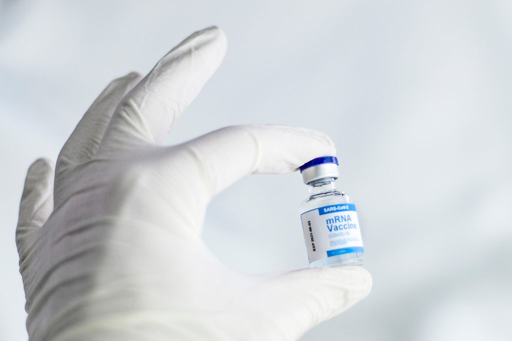 A white gloved left hand holds a small glass vial containing doses of the pfizer covid-19 vaccine.