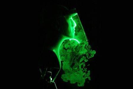 Green lasers pointed at a plastic mannequin head wearing a face shield show how the droplets from a cough or sneeze escape around the sides. 
