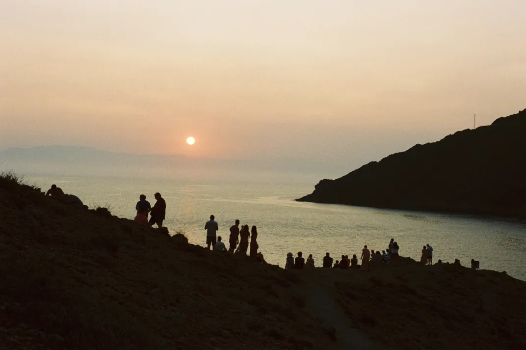 a crowd gathers to watch the sun setting on the sea
