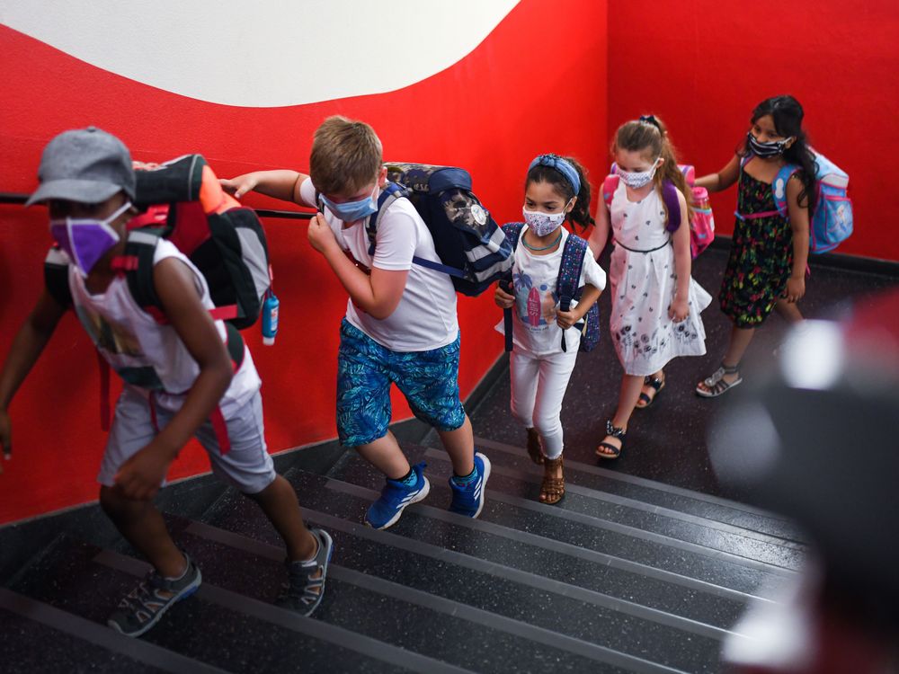 A row of children wearing masks walk up a staircase in a school.
