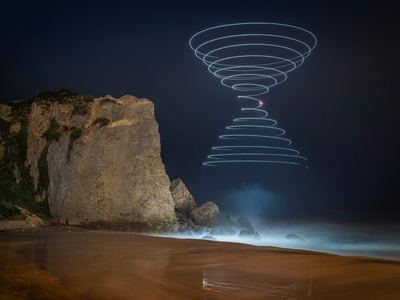 A three-to-four-minute exposure captures the light of a drone as it traces the shape of two cones in the sky along California&#39;s coast.