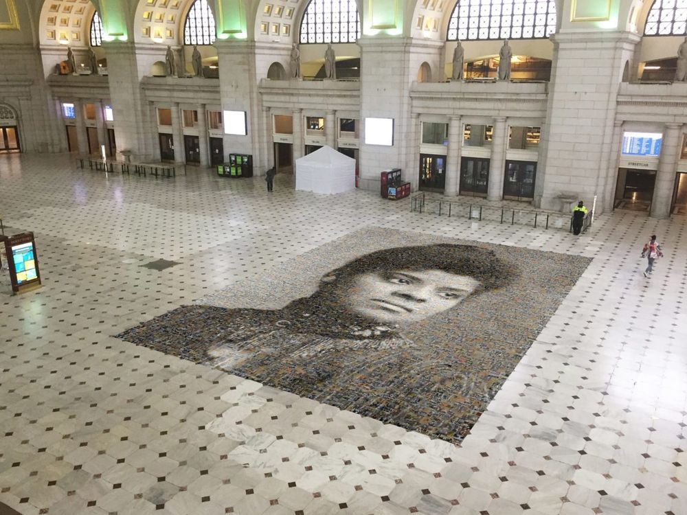 An aerial view of the mosaic, with two people walking nearby for scale; the mosaic takes up 1,000 square feet of floor in Union Station. The station is currently mostly empty due to the Covid-19 pandemic. 