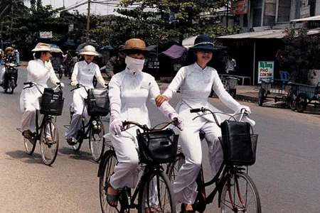 Ao dais make striking uniforms for four university students heading home after classes. Long gloves and hats provide welcome protection from the sun in a land where a suntan is not considered fashionable; masks serve as barriers to dust and exhaust.