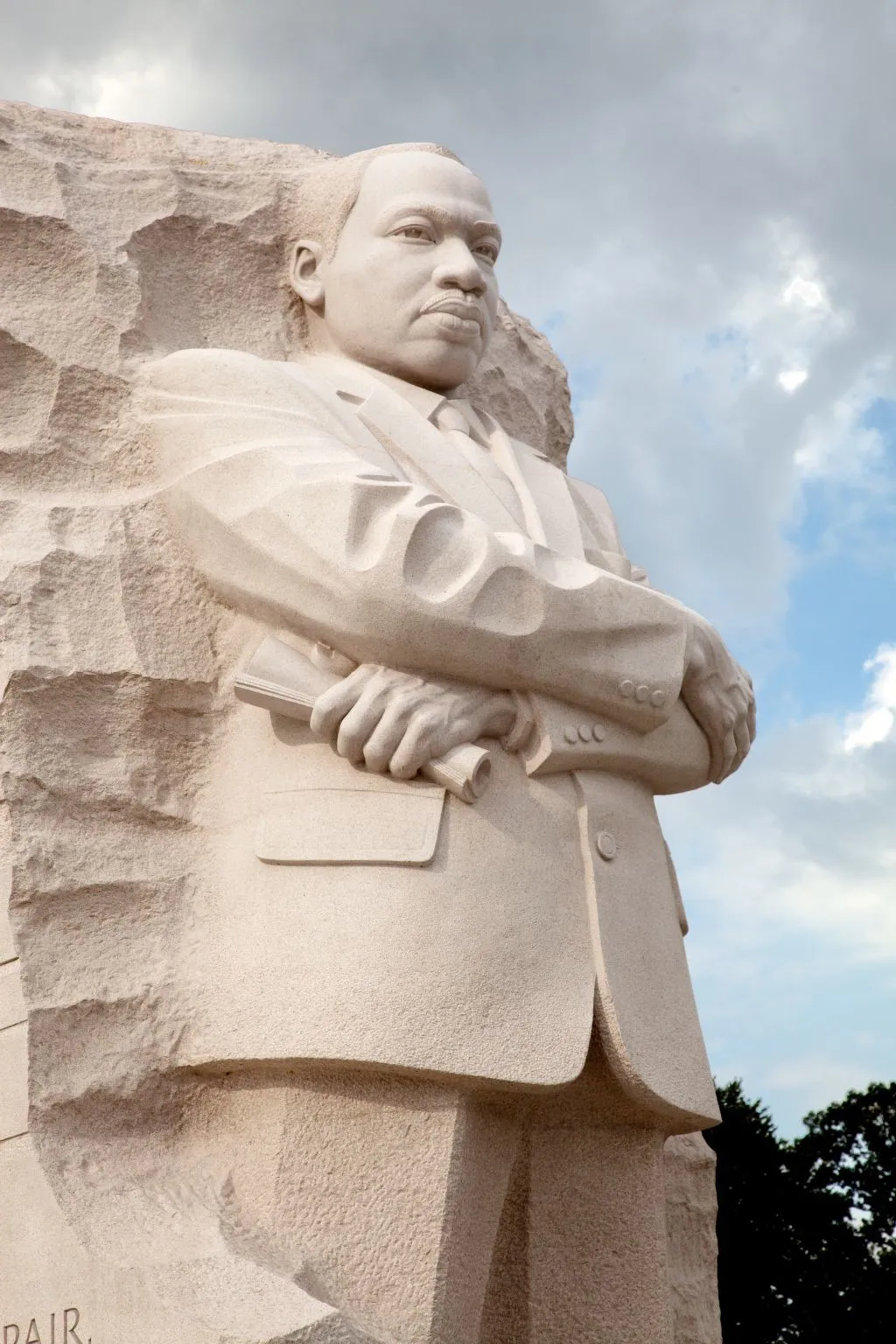 A carved white statue of MLK Jr, who stands tall with his arms crossed across his chest