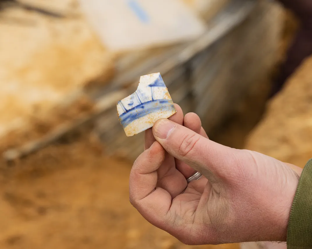 Person's hand holding up a fragment of blue and white ceramic