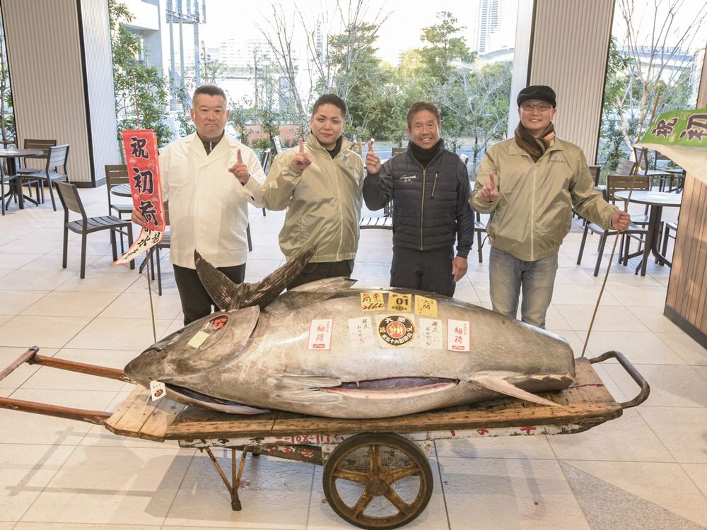 A giant fish on a rolling cart with four people standing behind it holding up their index finger in a No. 1 sign