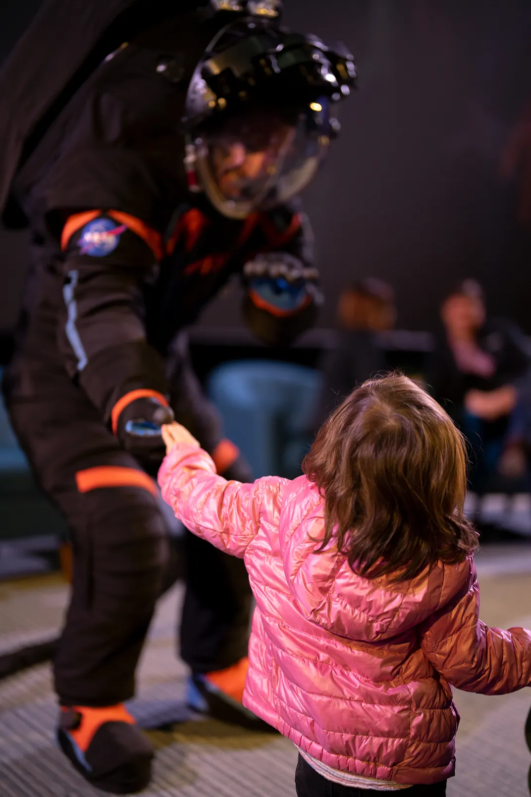 Man in spacesuit shaking hands with little girl in pink coat