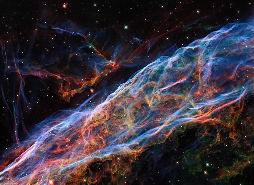 An astronomical image of the Veil Nebula. It is shown in various interweaving filaments of color. 