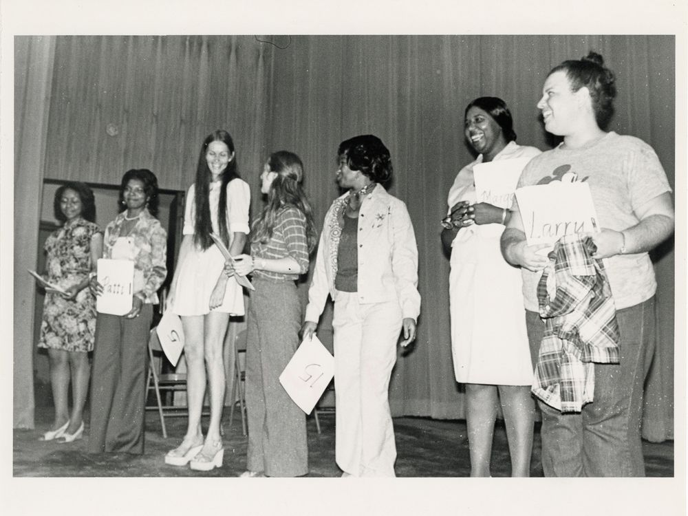 Candid photo of seven women holding papers standing in a line on stage.