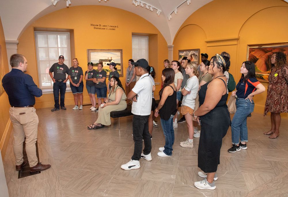 A man in a navy blue shirt and khakis leads a large group of students through an art gallery