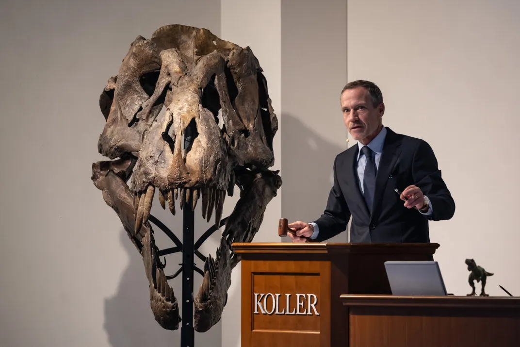 An auction house director stands next to a dinosaur skull