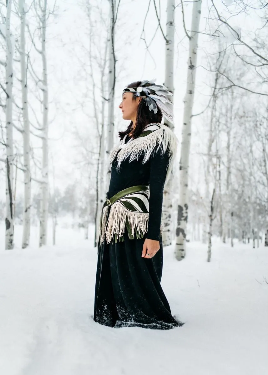 a model wears a black shawl and wrap with white tassels, and a feathered headdress