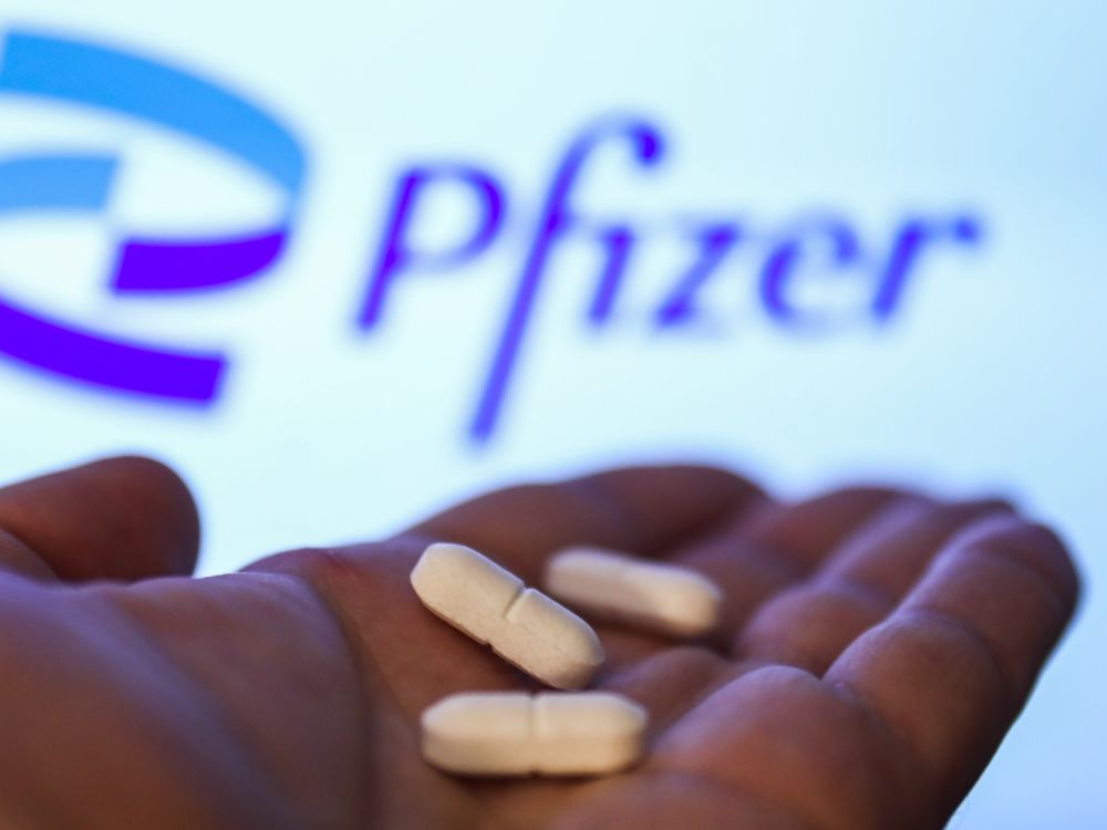 Hand holding three while tablet pills against Pfizer branded backdrop