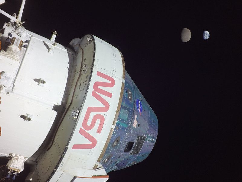 A photograph featuring the conical silver Orion spacecraft and cylindrical European Service Module in the foreground as it travels through space. In the background the Moon and then the Earth can be seen in the far distance.