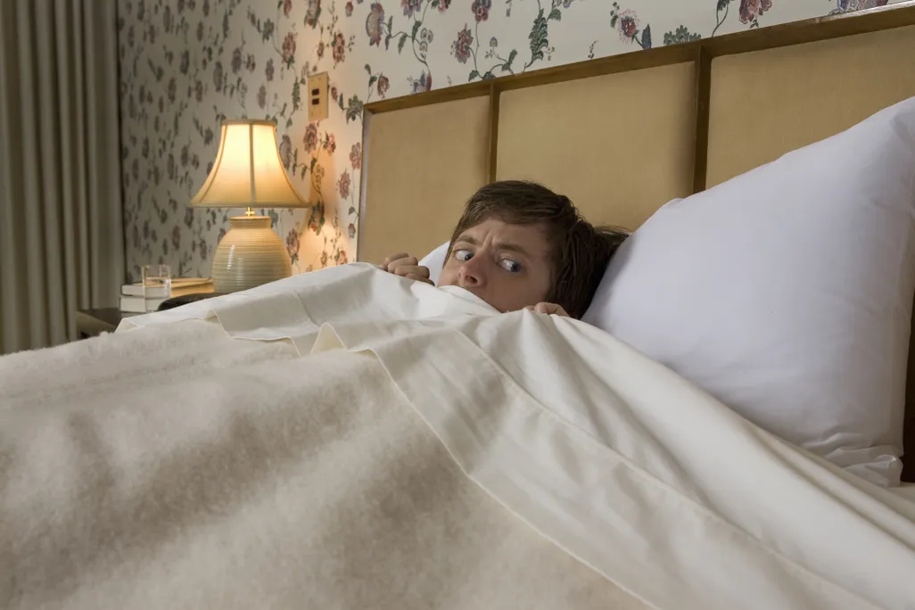 Man in bed with covers pulled up looking scared