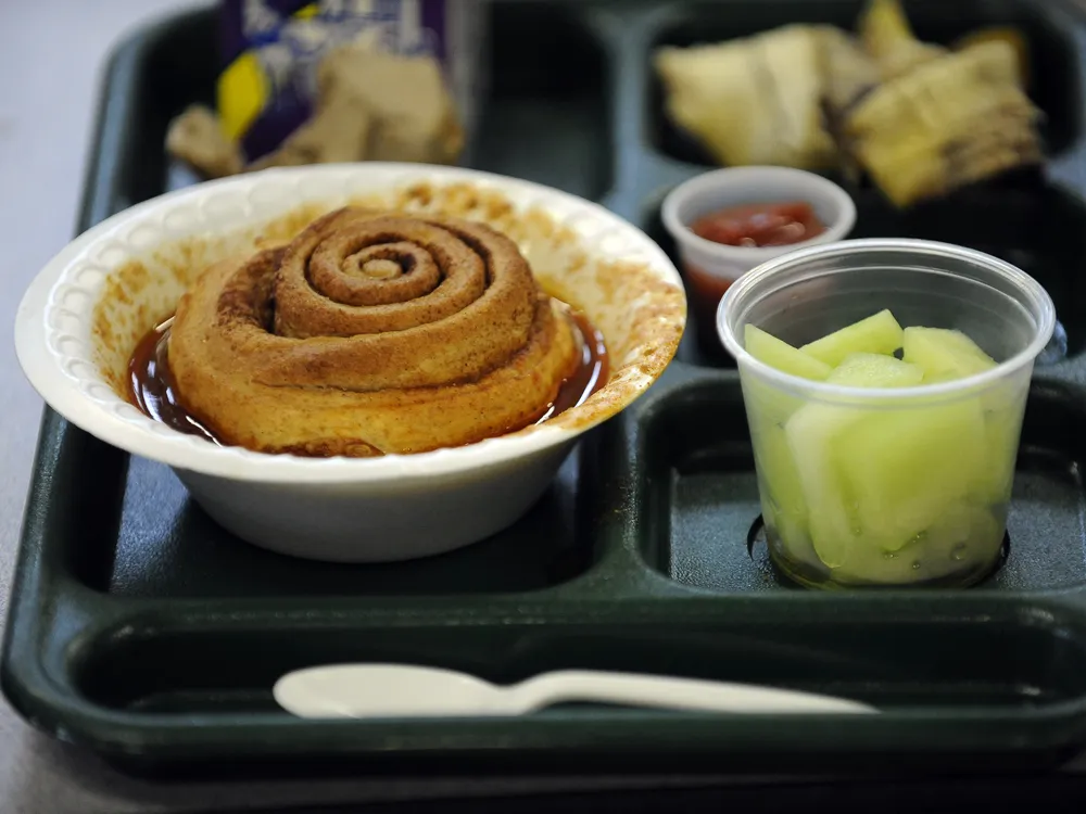 A cup of chili topped with a cinnamon roll on a school lunch tray