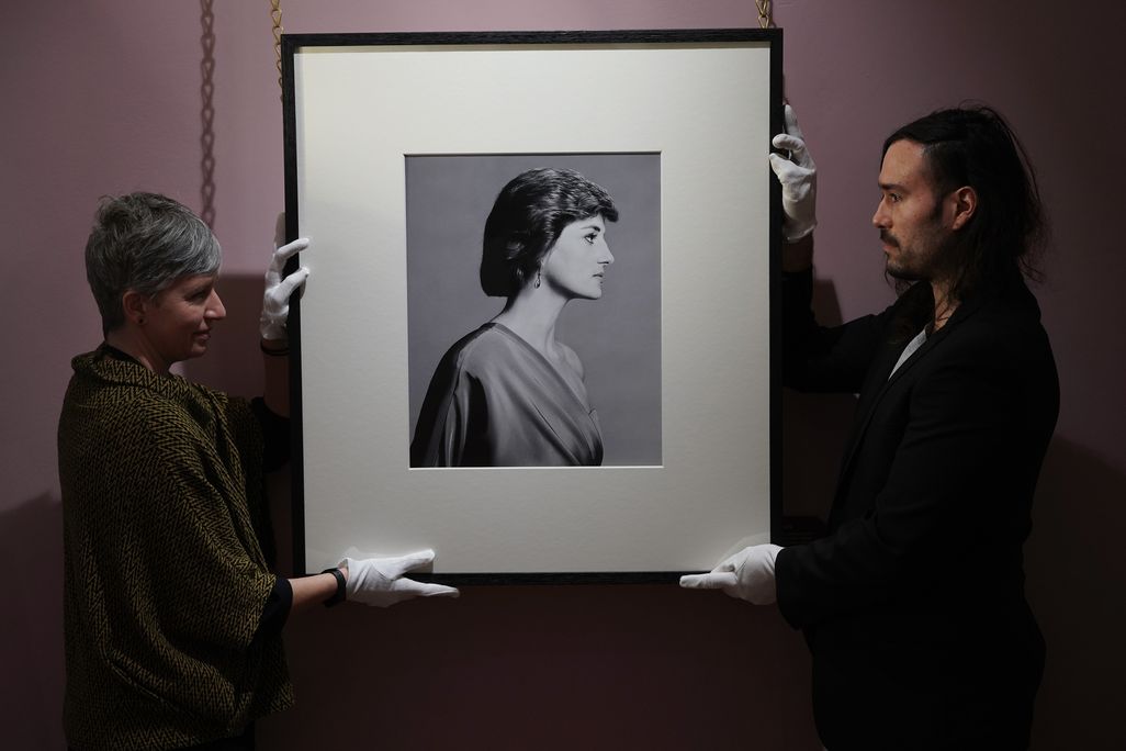 Two curators hanging up black and white portrait featuring profile of Princess Diana